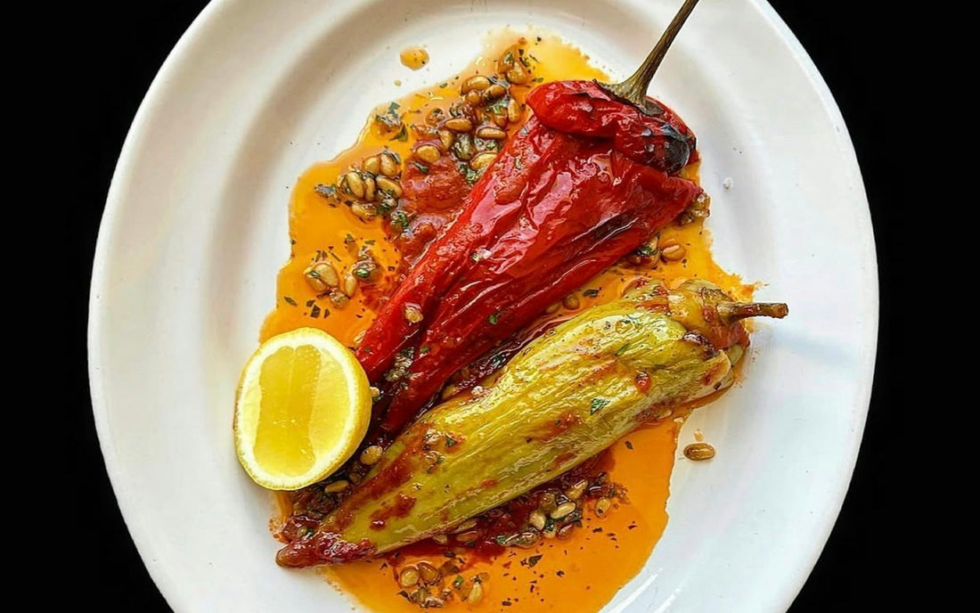 Charred and peeled sweet peppers on a white plate with olive oil, lemon and herbs