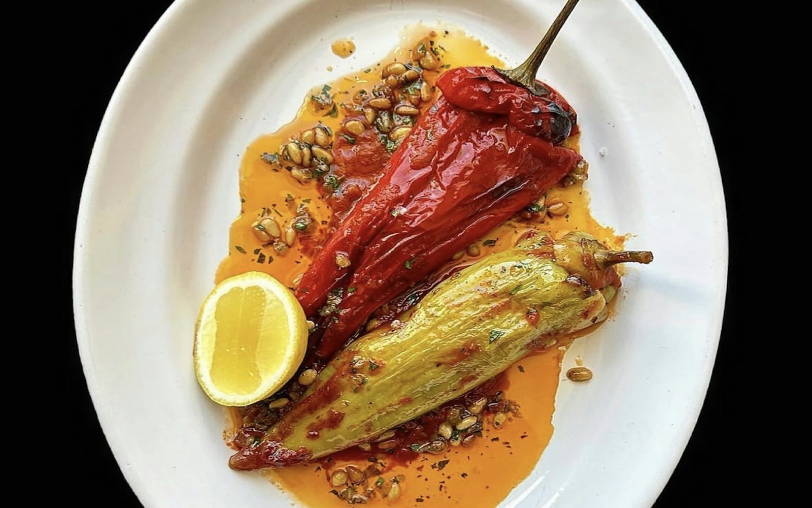 Charred and peeled sweet peppers on a white plate with olive oil, lemon and herbs